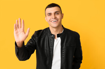 Handsome young man waving hand on yellow background