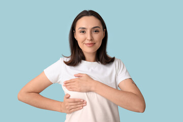 Young woman checking her breast on blue background. Cancer awareness concept