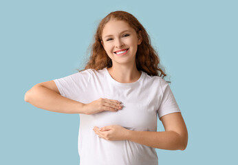 Young woman checking her breast on blue background. Cancer awareness concept