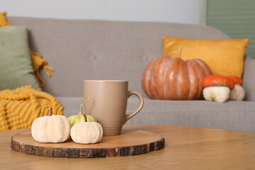 Obraz na płótnie Canvas Wooden coffee table with cup of tea and pumpkins in living room, closeup