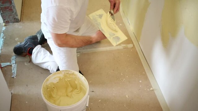 Worker is standing on the knee and decorating wall.