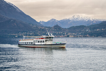 Ferry boat sails on Lake Como against the backdrop of a snow-covered mountain range