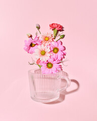 Floral composition with spring garden flowers and glass cup for tea on a candy pink background.