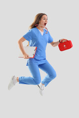 Shocked female medical intern with first aid kit and clipboard jumping on light background