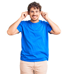 Fototapeta premium Young handsome man with curly hair wearing casual clothes smiling pulling ears with fingers, funny gesture. audition problem