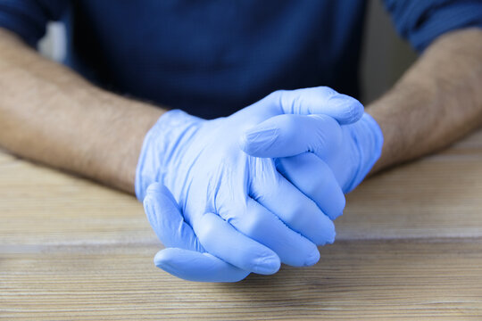 Clasped hands of doctor or nurse wearing latex gloves on wooden office table.
