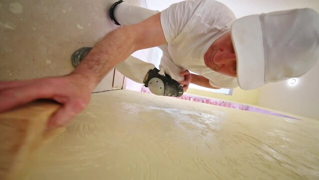 Worker in white cap is polishing yellow plaster wall.