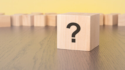 question mark written on wooden block lying on brown table, business and education concept. yellow...