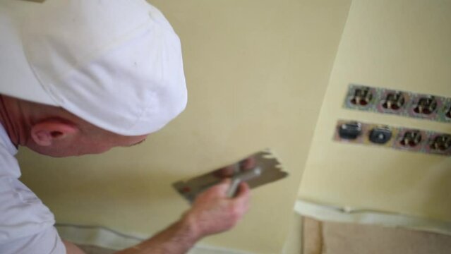 Worker in white uniform evens plaster wall using the trowel.