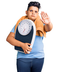 Little boy kid holding weight machine to balance weight loss with open hand doing stop sign with...