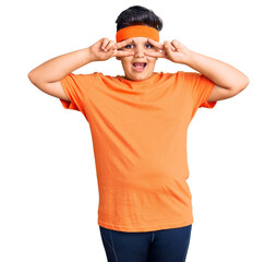 Naklejka premium Little boy kid wearing sportswear doing peace symbol with fingers over face, smiling cheerful showing victory