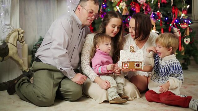 Family of five eats gingerbread house near Christmas tree