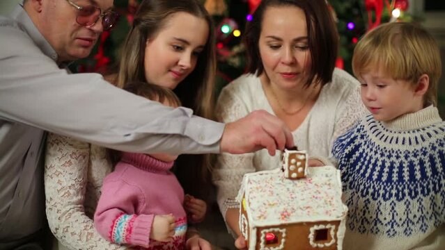 Happy family of five eats gingerbread house near Christmas tree
