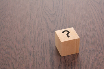 one wooden block with question mark over a brown background with copy space