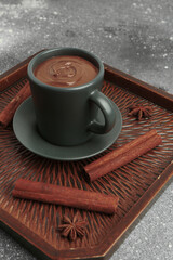Wooden board with cup of tasty melted chocolate and spices on grunge grey background, closeup
