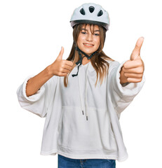 Teenager caucasian girl wearing bike helmet approving doing positive gesture with hand, thumbs up smiling and happy for success. winner gesture.
