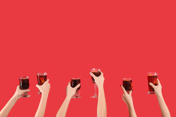 Female hands with glasses of warm mulled wine on red background