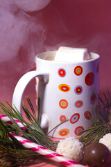 Coffee with marshmallows in a mug for a festive evening at the New Year's celebration. Keep warm in winter. Decoration pine branch, chocolate balls for Christmas candy cane.