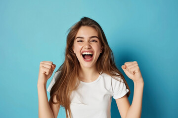 Photo of a young cheerful excited girl, rejoicing in success, with fists in her hands, isolated on a blue background