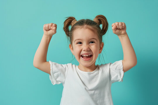 Photo of happy adorable cute little girl winner raising her fists and smiling, isolated on a pastel turquoise background