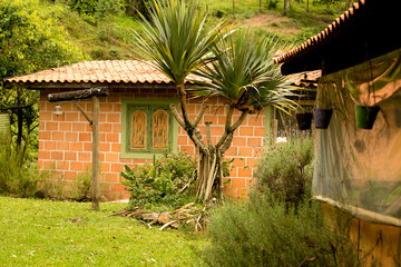 Fototapeta na wymiar Casa de alvenaria, parede de tijolo a vista, telhado de telha de barro, plantas e flores no jardim. Serra do japi, Jundiaí, São Paulo, Brasil. 