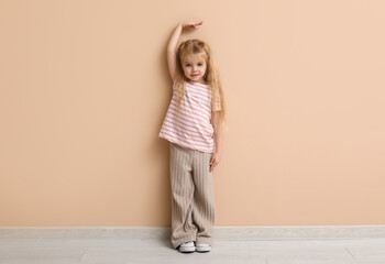 Cute little girl measuring height near beige wall