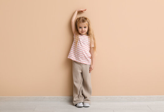 Cute little girl measuring height near beige wall