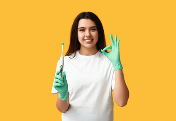 Female dentist with electric toothbrush showing ok gesture on yellow background. World Dentist Day