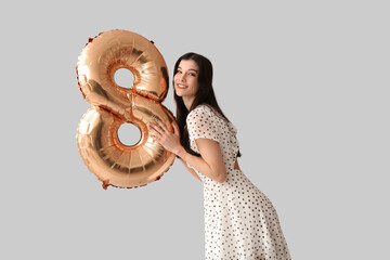 Naklejka premium Beautiful young woman with golden air balloon in shape of figure 8 on grey background. International Women's Day
