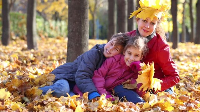 Mother and two children lie in autumn park with fallen foliage