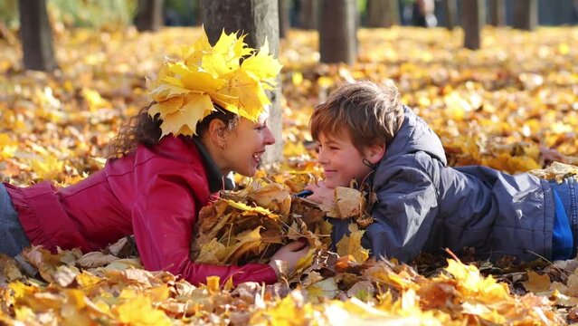 Smiling mother and son lie on yellow leaves in autumn park 