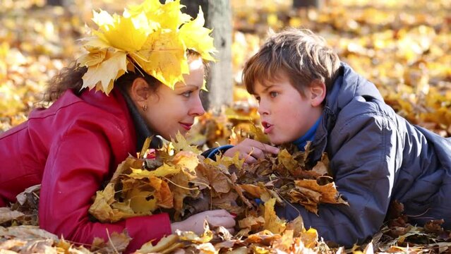 Mother and son lie on yellow leaves and talk in autumn park 