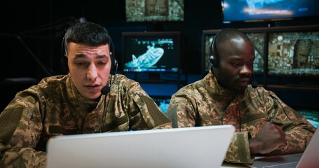 Multiethnic military men in uniforms and headsets talking and videochatting while working as...