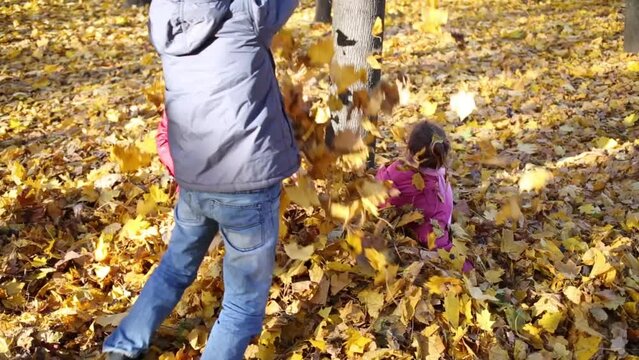 Mother and two children sit and throw yellow fallen leaves
