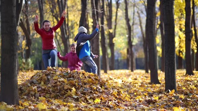 Mother and two children jump to big heap of yellow fallen leaves