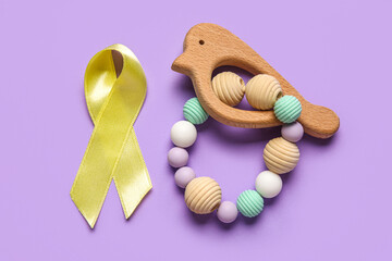Golden ribbon with rattle on lilac background. Childhood cancer awareness concept