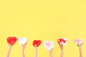 Female hands holding different heart-shaped gift boxes on yellow background. Valentine's Day celebration