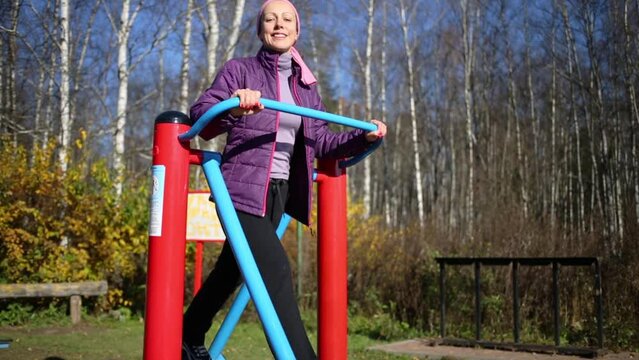 Young woman does exercises at simulator in park in autumn day