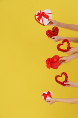 Female hands holding heart-shaped gift boxes and hearts on yellow background. Valentine's Day celebration