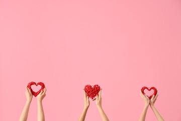 Female hands holding decorative hearts on pink background. Valentine's Day celebration