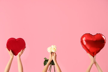 Female hands holding heart-shaped balloon, gift box and roses on pink background. Valentine's Day...