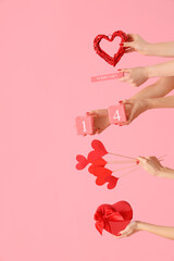 Female hands holding cube calendar with date 14 FEBRUARY, gift box and hearts on pink background....