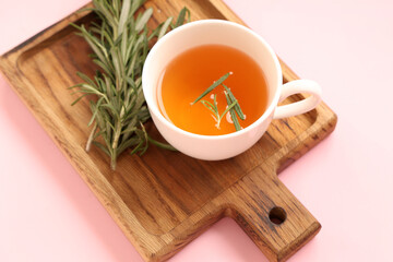 Wooden board with cup of hot rosemary tea on pink background