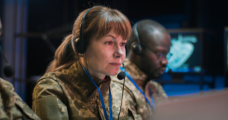 Multiethnic male and female military dispatchers in camouflage uniforms and headsets working at...