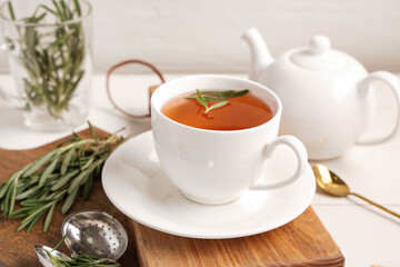 Board with cup and teapot of hot rosemary tea on white wooden table