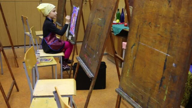 Little girl is sitting in the classroom and painting.