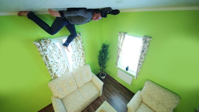 Man in jeans lies on ceiling above sofa without shoes and socks 