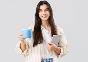Beautiful young woman with mug of tea and tablet computer on grey background