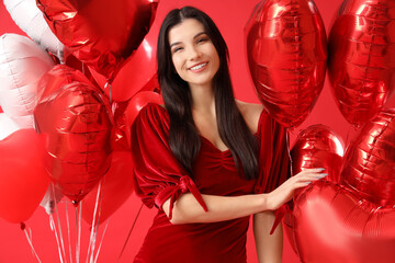 Beautiful young woman with heart-shaped air balloons on red background. Valentine's day celebration