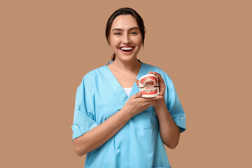 Young female dentist with jaw model on beige background
